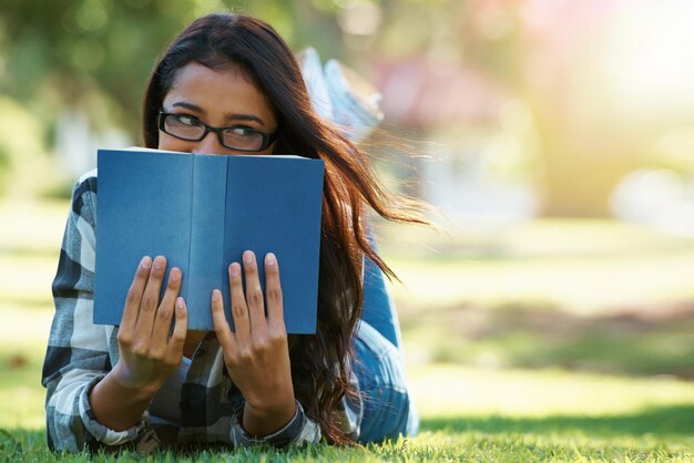 Kobieta studentka leżąca z książką na zielonej trawie do studiowania literatury lub opowieści w przyrodzie Kobieta nerd lub młody geek z notatnikiem do czytania edukacji lub tajemnicy przyszłości w parku