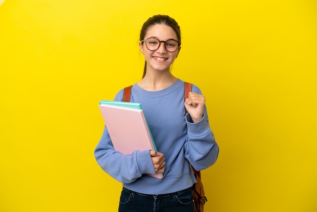 Kobieta-studentka na odosobnionym żółtym tle świętuje zwycięstwo w pozycji zwycięzcy