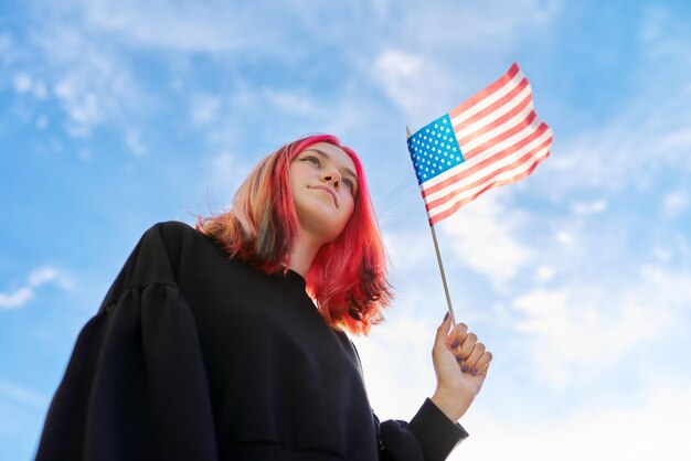 Kobieta studentka nastolatka z flagą USA w ręku, błękitne niebo z chmurami w tle. Stany Zjednoczone Ameryki, edukacja i młodzież, koncepcja ludzie patriotyzmu