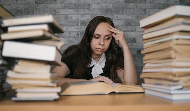 Kobieta studentka nudna książka do czytania w bibliotece z dużą ilością książek na uniwersytecie Student zniechęcony czytaniem książki do egzaminu