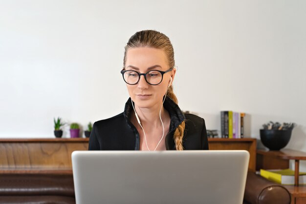 Kobieta studiuje pracę online w okularach i słuchawkach i laptopie
