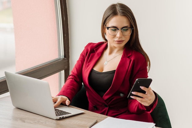 Kobieta sukcesu, ubrana w czerwoną kurtkę, pracuje z laptopem w biurze