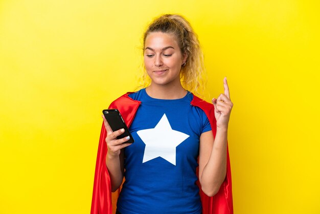 Kobieta Super Hero na żółtym tle za pomocą telefonu komórkowego i podnosząc palec