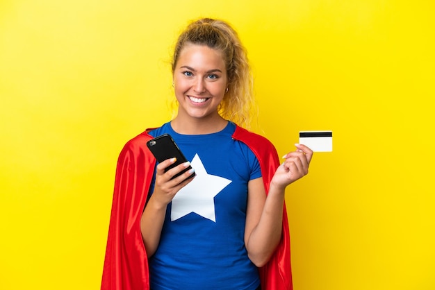 Kobieta superbohater na żółtym tle kupując za pomocą telefonu komórkowego za pomocą karty kredytowej