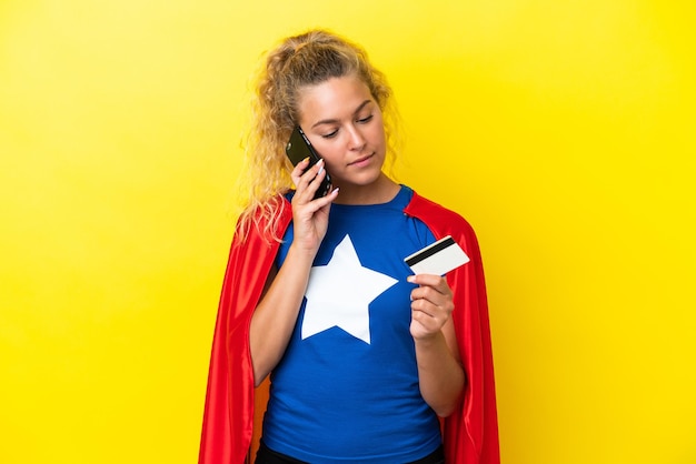Zdjęcie kobieta superbohater na żółtym tle kupując za pomocą telefonu komórkowego za pomocą karty kredytowej