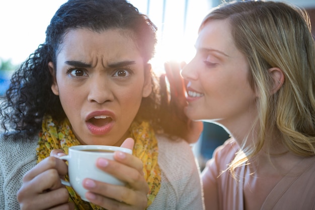 Kobieta szepcząc sekret do ucha przyjaciół podczas picia kawy
