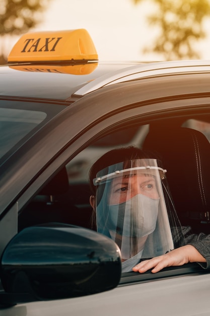 Zdjęcie kobieta taksówkarz z maską ochronną i plastikowym daszkiem czeka w samochodzie