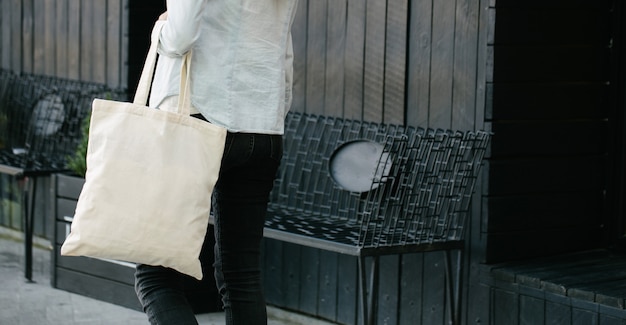 Kobieta trzyma białą tekstylną eko torbę na tle miejskiego miasta. . Koncepcja ekologii lub ochrony środowiska. Biała eko torba na makiety.