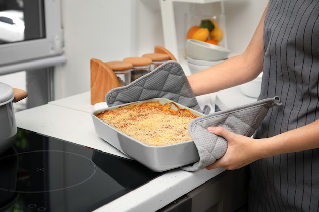 Kobieta trzyma blachę do pieczenia ze szpinakową lasagne w kuchni