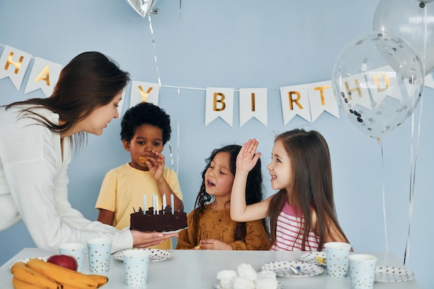 Zdjęcie kobieta trzyma ciasto dzieci na przyjęciu urodzinowym w domu bawią się razem