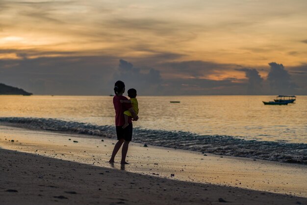 Kobieta trzyma dziecko na plaży o zachodzie słońca.