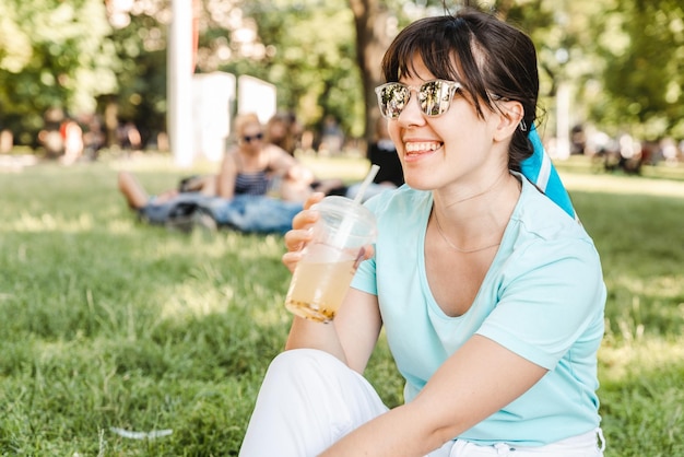 Kobieta trzyma fajny napój w parku miejskim rozmazane tło szeroki anioł