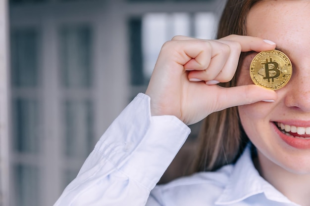 Kobieta trzyma fizyczną kryptowalutę bitcoin w dłoni zakrywającej oko
