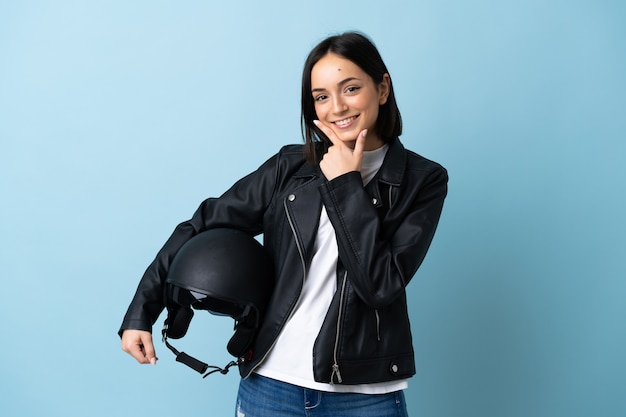 Kobieta trzyma kask motocyklowy na białym tle na niebieskim tle szczęśliwa i uśmiechnięta