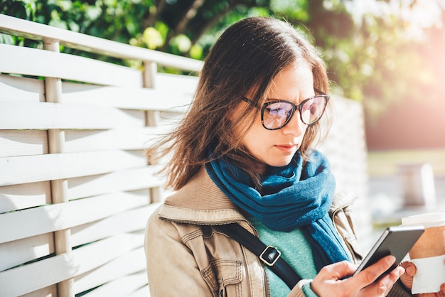 Kobieta trzyma kawę na wynos i używa mądrze telefon