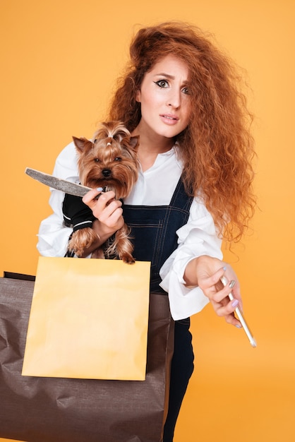 Kobieta trzyma ładny yorkshire terrier i telefon komórkowy na pomarańczowej ścianie