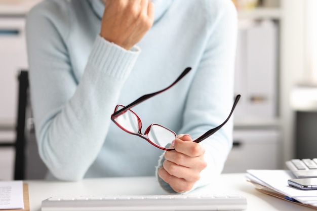 Kobieta trzyma okulary w rękach siedząc w miejscu pracy. Noszenie okularów w koncepcji pracy