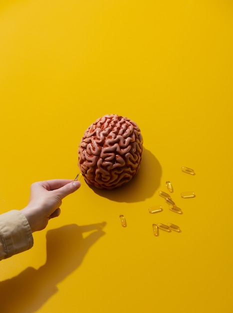 Kobieta trzyma pigułki w pobliżu mózgu na żółtej powierzchni