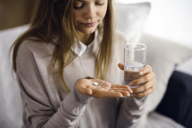 Kobieta trzyma pigułki z bliska, czas na zażywanie leków, lekarstwo na ból głowy, wysokie ciśnienie krwi lub poziom cholesterolu, leki przeciwbólowe. Koncepcja pozostania w domu podczas pandemii koronawirusa i samo-i