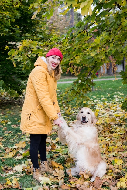 Kobieta trzyma psa za przednie łapy. Młoda dziewczyna spacerująca ze swoim aporterem wśród jesiennych żółtych liści