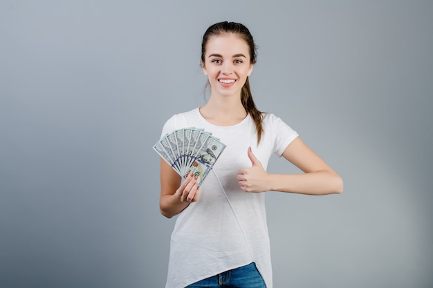 Kobieta trzyma setki dolarów i pokazuje aprobaty odizolowywać nad popielatym