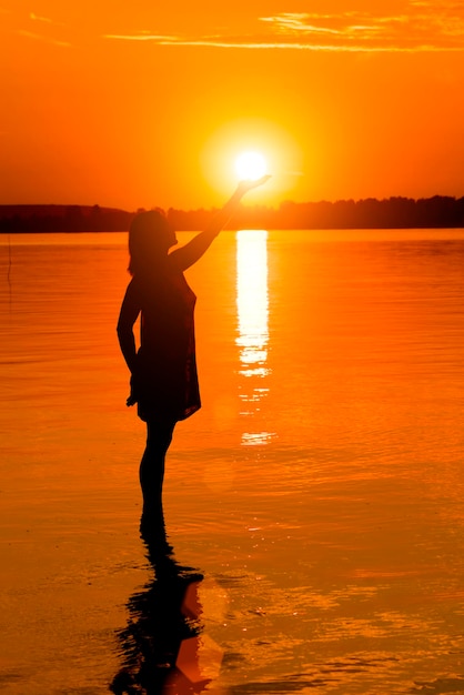Kobieta trzyma słońce w wodzie o zachodzie słońca