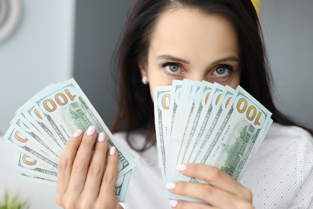 Kobieta trzyma stu dolarowe rachunki na poziomie twarzy