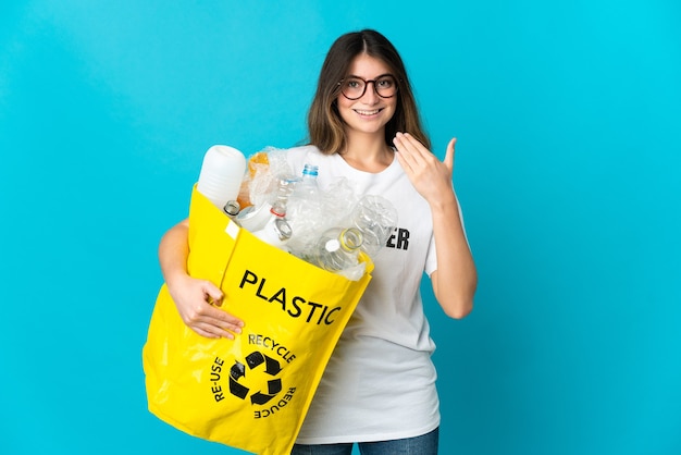 Kobieta Trzyma Torbę Pełną Butelek Do Recyklingu Na Białym Tle Na Niebiesko, Zachęcając Do Przyjścia Z Ręką