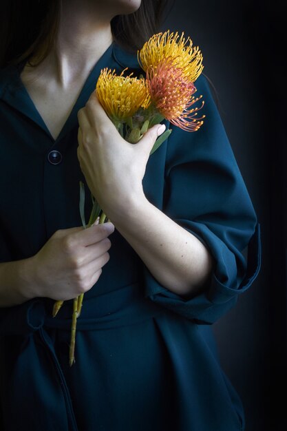 Kobieta trzyma trzy żółte i pomarańczowe proteas