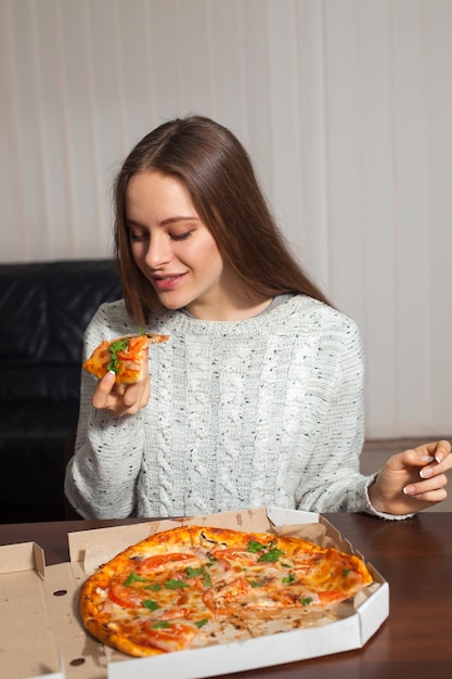 Kobieta trzyma w dłoni kawałek pizzy i chce go zjeść