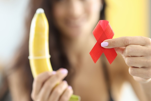 Kobieta trzyma w dłoniach banana z prezerwatywą i czerwoną wstążką