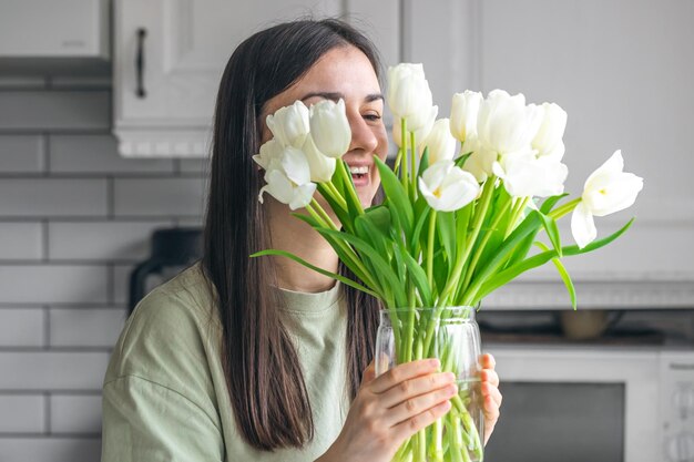 Kobieta trzyma wazon z białymi tulipanami w wnętrzu kuchni