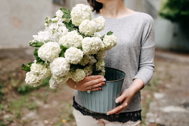 Kobieta trzyma wiadro z sezonowymi białymi kwiatami