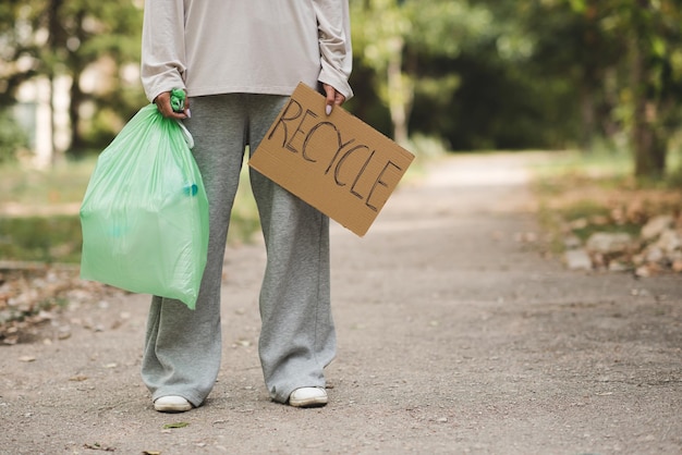 Kobieta trzyma zieloną plastikową torbę ze śmieciami i tabletem ze znakiem recyklingu na zewnątrz Dziewczyna pomaga w czyszczeniu środowiska