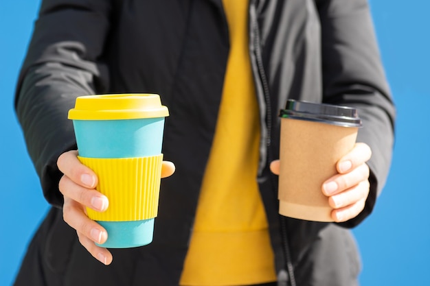 Kobieta trzymająca ekologiczny kubek do kawy w obu rękach, jedna to papierowy kubek jednorazowego użytku.