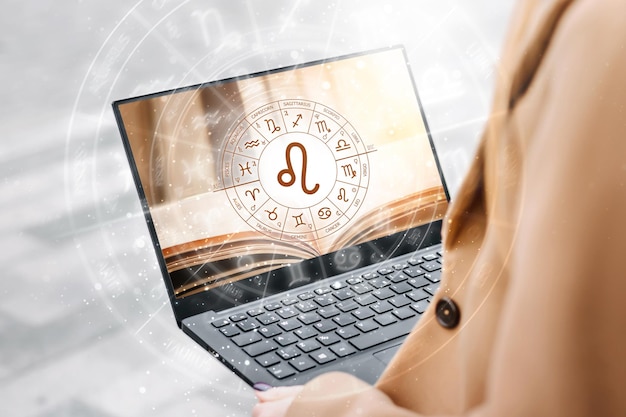 Kobieta trzymająca otwartego laptopa ze zdjęciem książki i okręgiem zodiaku