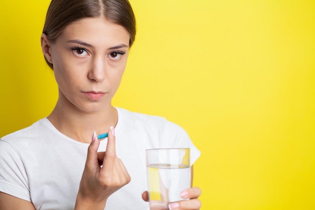 Kobieta trzymająca pigułkę i szklankę wody zażywająca suplementy diety