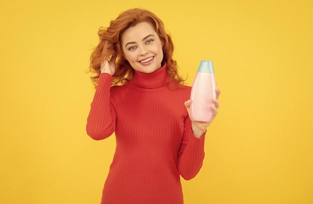 Kobieta trzymająca szampon i odżywkę Rude kręcone włosy Kobieta trzymająca butelkę organicznego szamponu Piękna ruda dziewczyna z butelką szamponów w rękach Dziewczyna z lśniącymi kręconymi długimi włosami