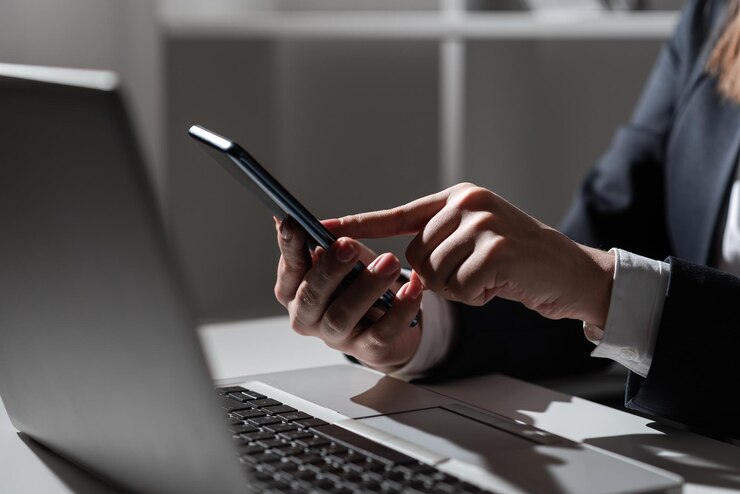 Kobieta trzymająca tablet w jednej ręce i wskazująca go jednym palcem na biurku na kolanach Siedząca kobieta w biurze z telefonem komórkowym w ręku prezentująca informacje