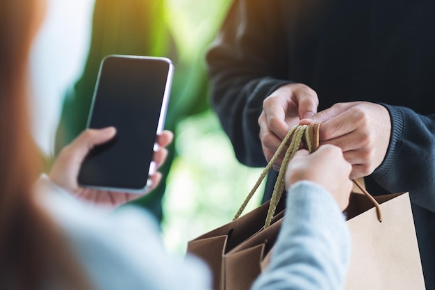 Kobieta trzymająca telefon komórkowy i odbierająca torby na zakupy od doręczyciela