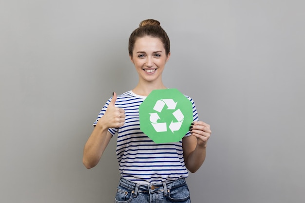 Kobieta trzymająca w dłoni zielony znak recyklingu i pokazująca kciuk w górę jak gest myślący na zielono