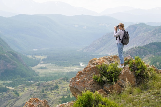 Kobieta Turysta Stojąca Na Szczycie Klifu W Letnich Górach I Patrząca W Lornetkę