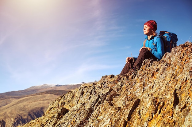 Kobieta turystka z plecakiem siedząca na skale góry i ciesząca się wschodem słońca