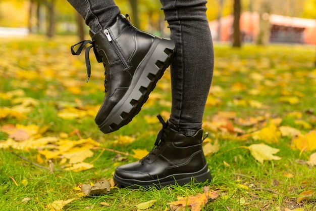 Kobieta ubrana w czarne buty z czarnymi sznurowadłami stoi na trawie w jesiennym parku.
