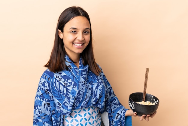 Kobieta ubrana w kimono i uśmiechnięta trzymając miskę makaronu