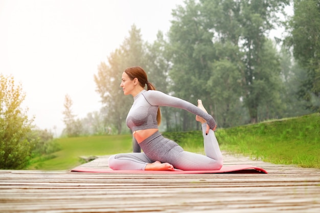 Kobieta ubrana w legginsy i top z różową matą robi jogę na letnim parku. Koncepcja zdrowego stylu życia sportowego