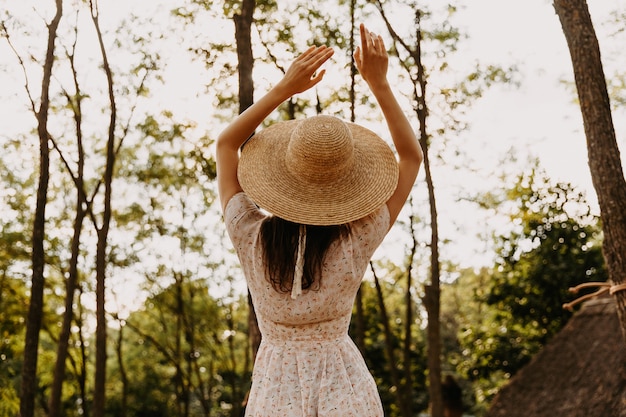 Kobieta ubrana w słomkowy kapelusz i letnią sukienkę w lesie
