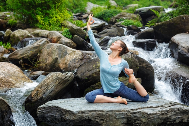 Kobieta uprawiająca jogę na świeżym powietrzu przy tropikalnym wodospadzie