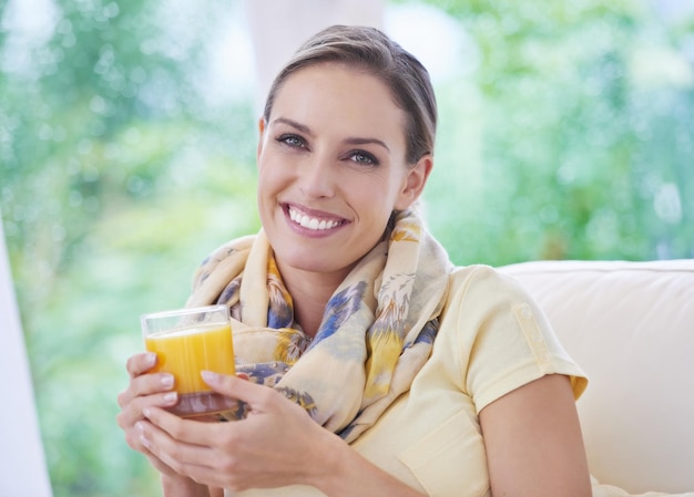 Kobieta uśmiech i sok pomarańczowy w szklanym portrecie lub zrelaksować się na kanapie w domowym salonie dla dobrego samopoczucia Osoba puncz owocowy i szczęśliwy z napojem dla diety odżywiania lub zdrowia na kanapie salonu w mieszkaniu
