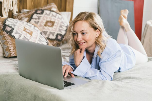 Kobieta uśmiecha się i patrzy na ekran laptopa.